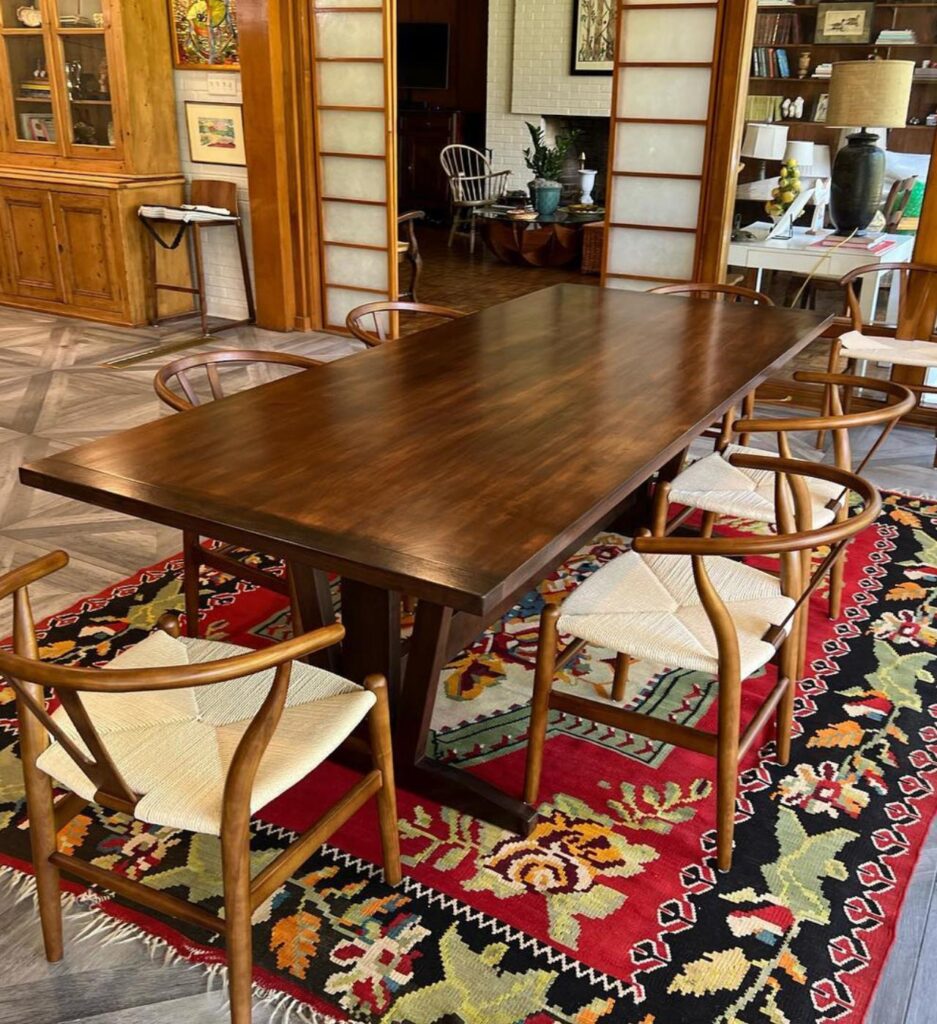 A beautifully crafted dining area by Francise Construction Services in Baton Rouge, including a rich wooden table and complementary chairs on a vibrant red and multicolored rug, against a backdrop of wood-paneled walls.