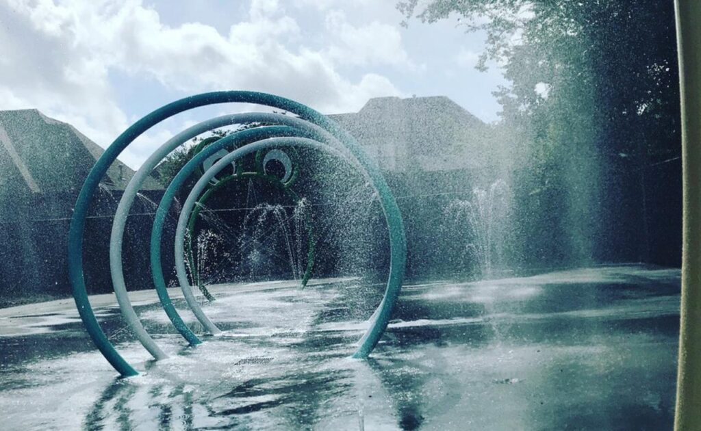 Sunlit splash pad with cascading water rings and wet ground, showcasing outdoor summer fun and family-friendly water play area.