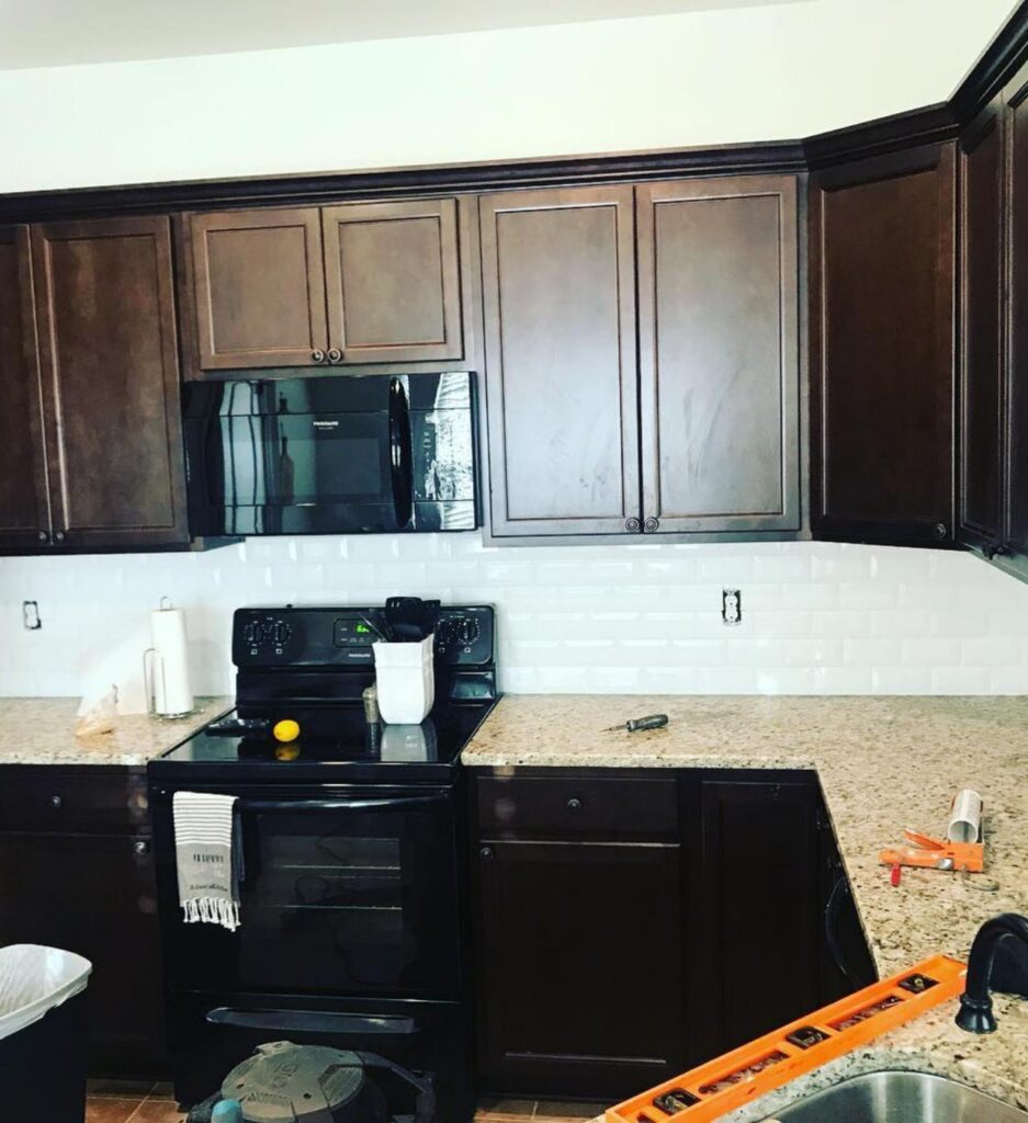 A modern kitchen by Francise Construction Services in Baton Rouge, featuring dark wooden cabinetry, granite countertops, and a white subway tile backsplash. The kitchen is under renovation with tools and equipment visible on the counters.
